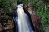 a steep rushing waterfall with rock and trees surrounding