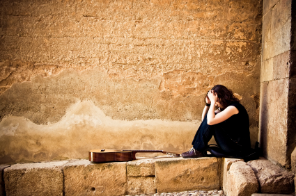 Lone female street artist against stonewall as background with guitar