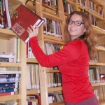 stacy balkun on ladder pulling of a book from a wall of shelves