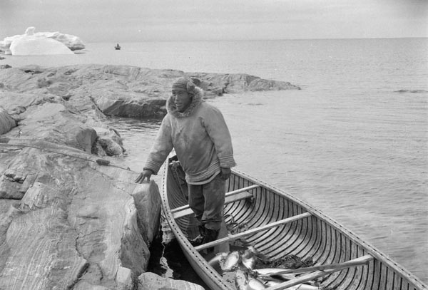 inuit man in canoe with fish with iceberg in back