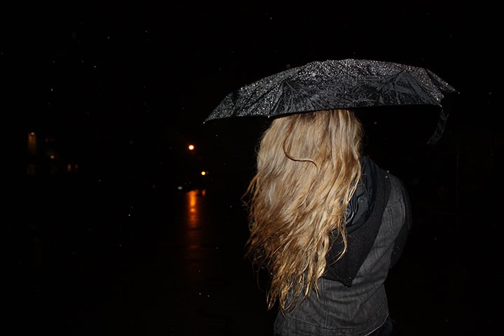 woman in rain under umbrella back facing camera