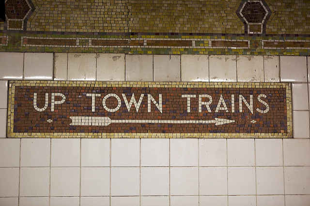 tiles on subway statopm wall and sign that says up town train with arrow pointing to the right