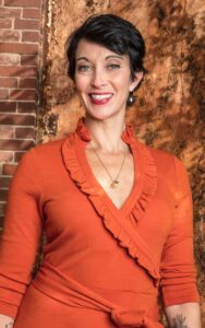 A woman in an orange dress stands in front of a wall