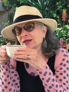 Megan Vered in pink and black polkadot top holding a cup of coffee or tea.