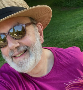 Headshot of a man wearing a straw hat and sunglasses