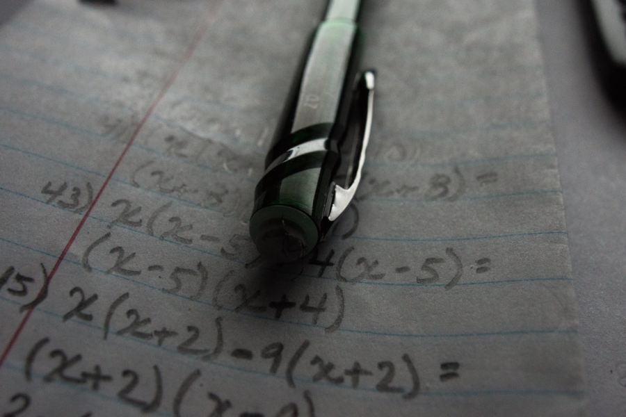 pen resting on spiral notebook page with algebraic equations