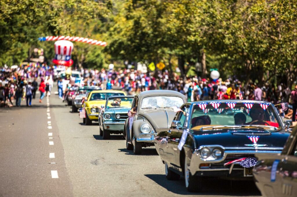 A group of classic cars on a road with a crowd watching -- parade 
