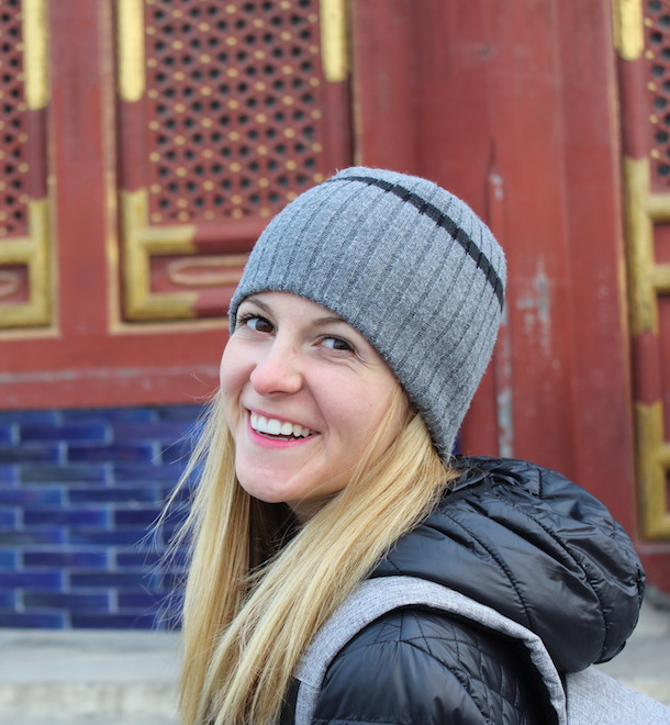 whitney brown in knit winter beanie and coat in front of colorful city scene