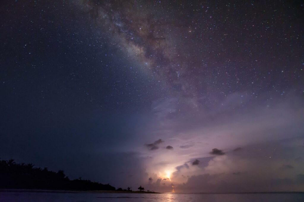 A night sky with stars and clouds, just over the water