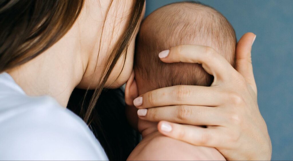 A person holding a baby, cradled in crook of their neck