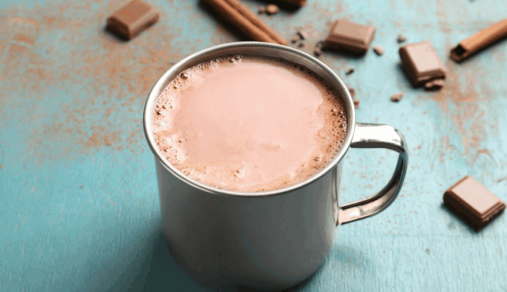 A mug of hot chocolate with pieces of cacao in the back