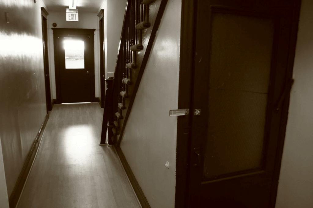 interior of apartment building, looking down hallway to exit w/ stairwell on the side