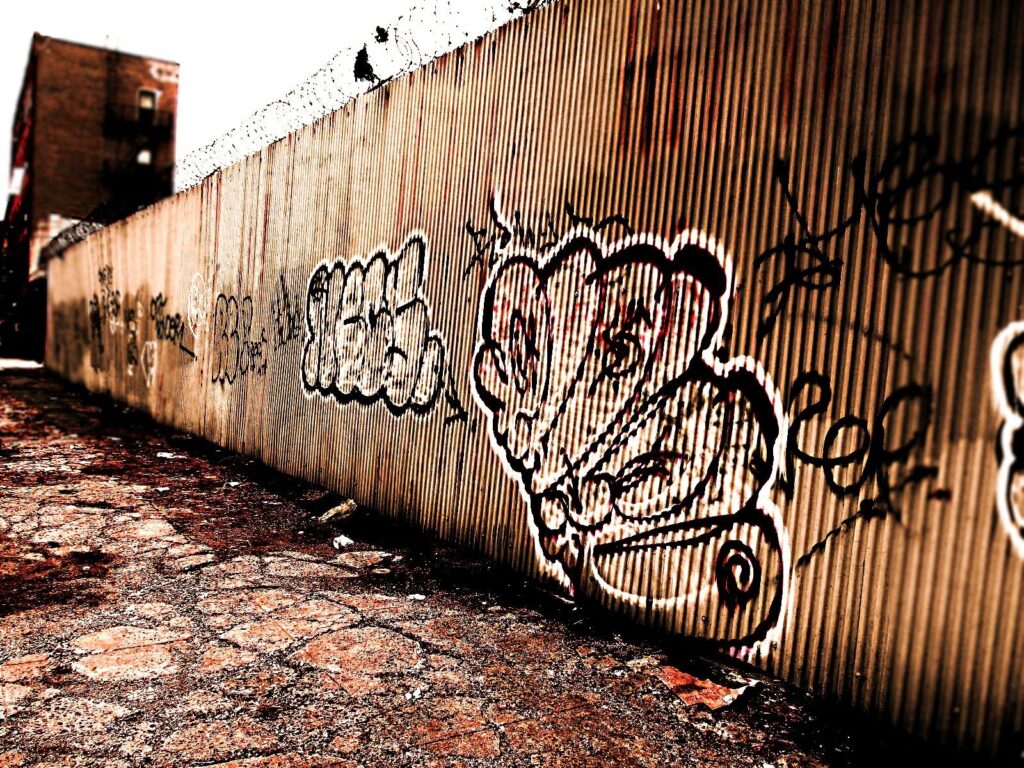 A metal wall with graffiti and barbed wire on top