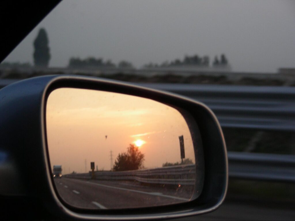 side-mirror of car with reflection of road behind at sunset