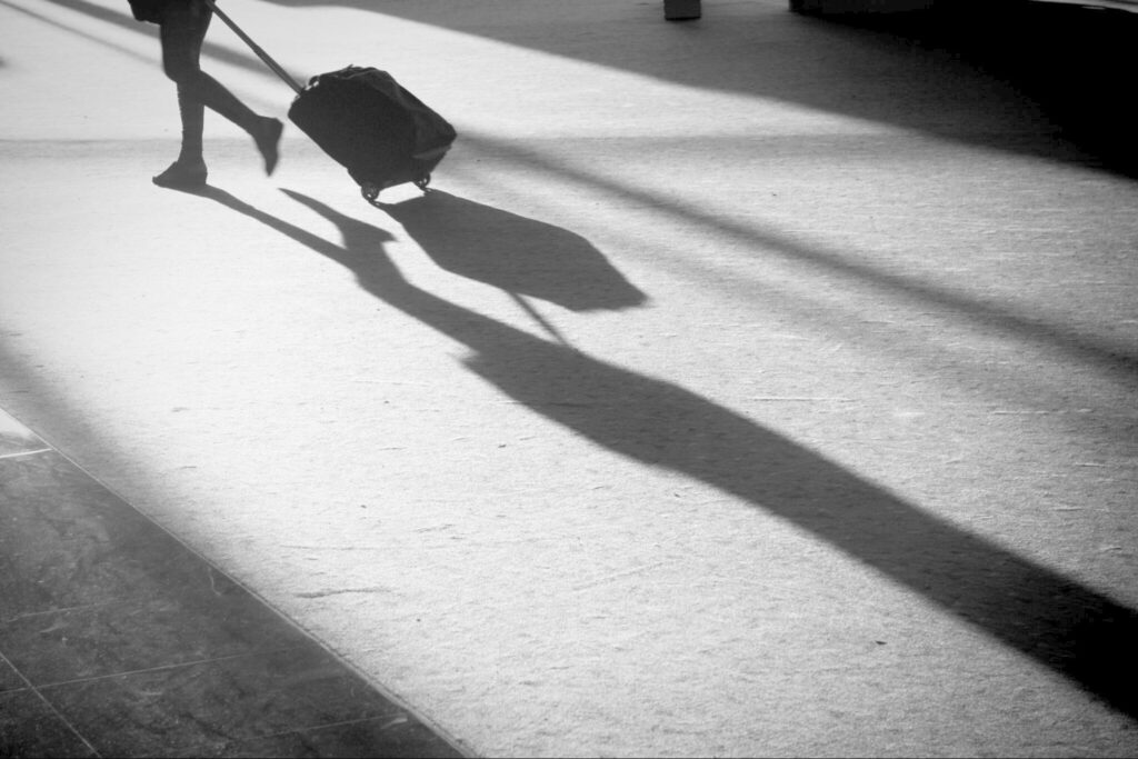 female pulling rolling carry-on through airport with shadow; only her legs showing in upper left frame