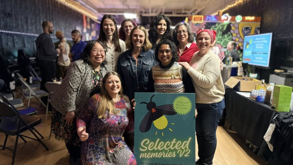 group of writers surrounding a life-size image of the book cover for selected memories vol. 2, right before the book launch party