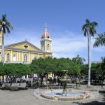 fountain in center of granada with palm trees and churc in background