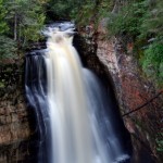 a steep rushing waterfall with rock and trees surrounding