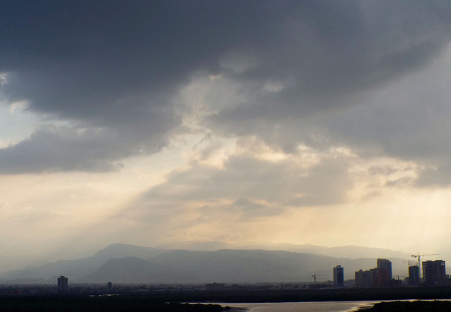 Dark rain clouds and rain with a little light peeking through over city in uae mountains in distance