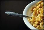 bowl of corn flakes off center, spoon sticking otu