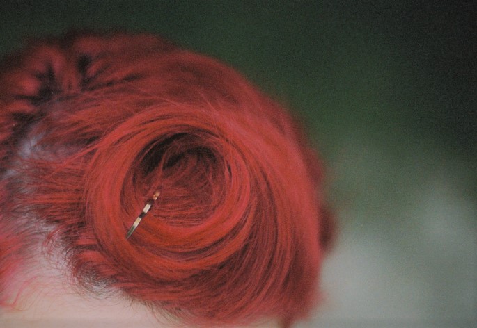 close-up shot of dyed bright red hair, with a wisp of curl bobby-pinned