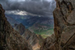 view of moutnains from higher up on a taller rocky landing, clouds in sky