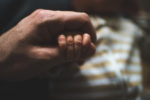 father's hand gently grapsing tiny baby hand