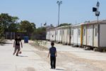 two boys kicking soccer ball at athens refugee camp with houses on right photo by international federation for the Red Cross and Red Crescent Societies