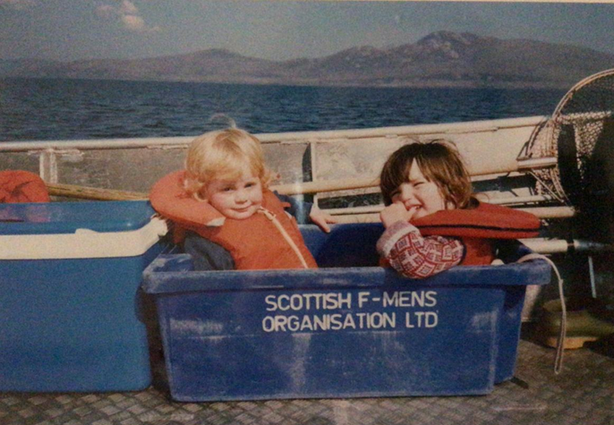Author and sibling as children in fishing boat sitting inside a salmon crate with life preservers on