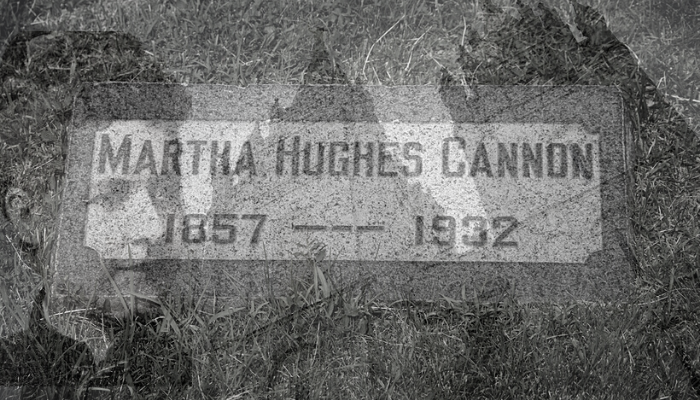 Martha hughes cannon's grave stone with both the mormon temple and image of marie blurred in background, almost shadows