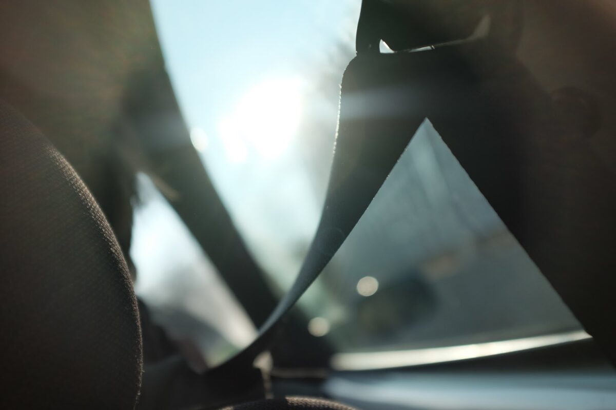 close-up shot of a seatbelt and sun glaring into a car window