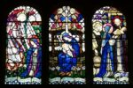 A stained glass windows, three panels each depicting groups of people, including mary and baby jesus