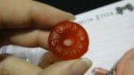 A hand holding a red round candy (a Lifesaver)