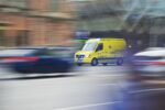 A yellow ambulance on the road with the rest of the traffic blurred out to indicate speed and motion