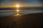 A sunset over a beach with footprints in the sand