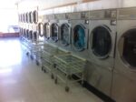 A row of washing machines in a laundromat with carts in front of them