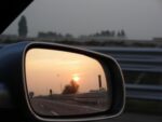 side-mirror of car with reflection of road behind at sunset