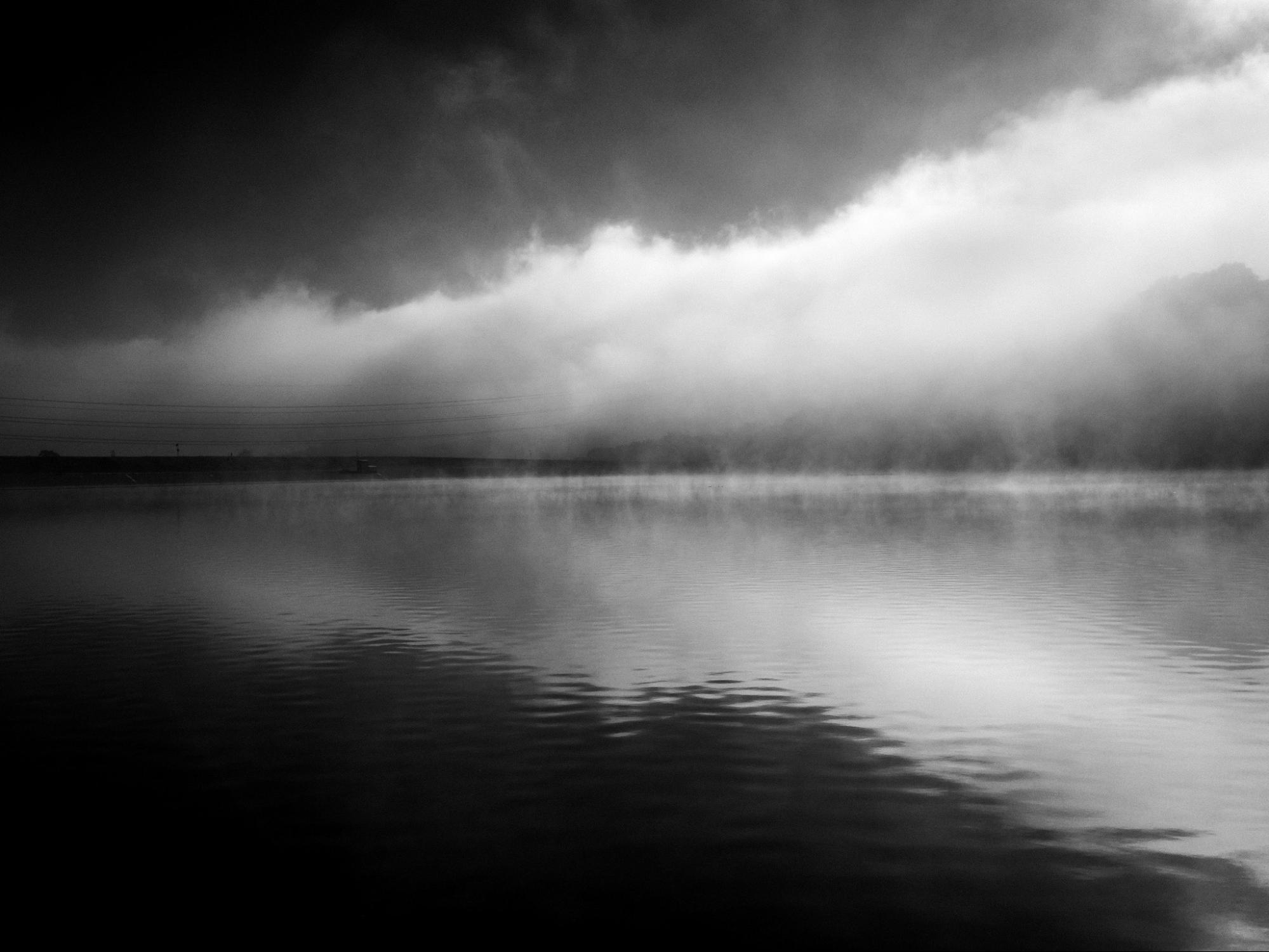 black and white image of a lake with puffy white clouds above