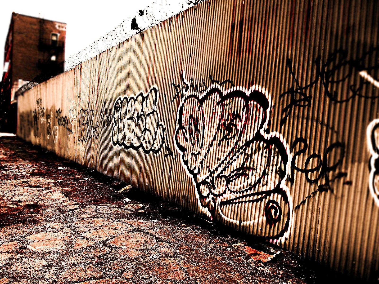 A metal wall with graffiti and barbed wire on top