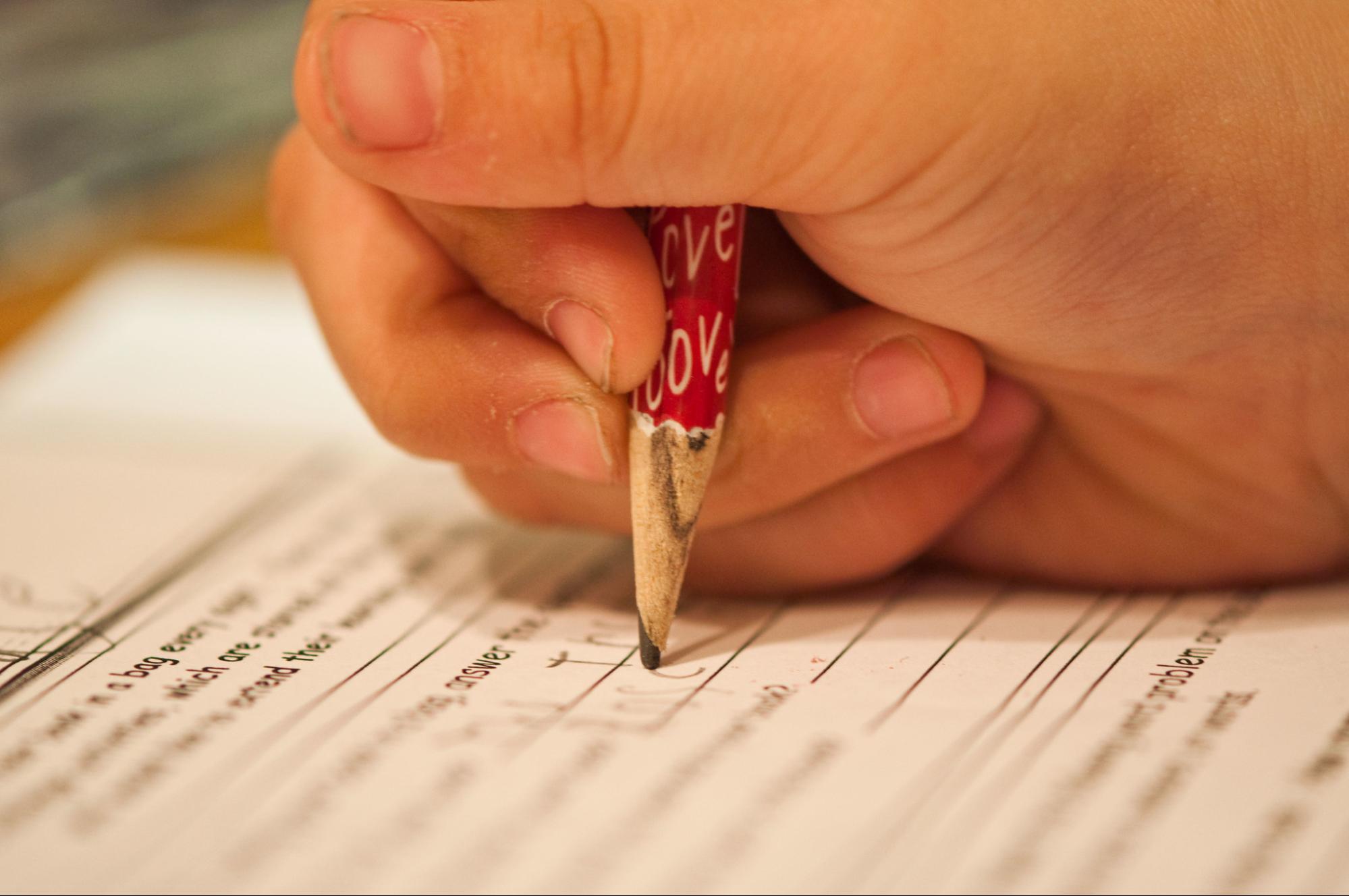 close-up of a child's hand holding a pencil, taking a test