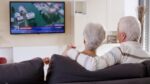 A gray-haired couple watching a television