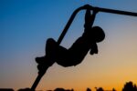 silhouette of child on money bars at sunset