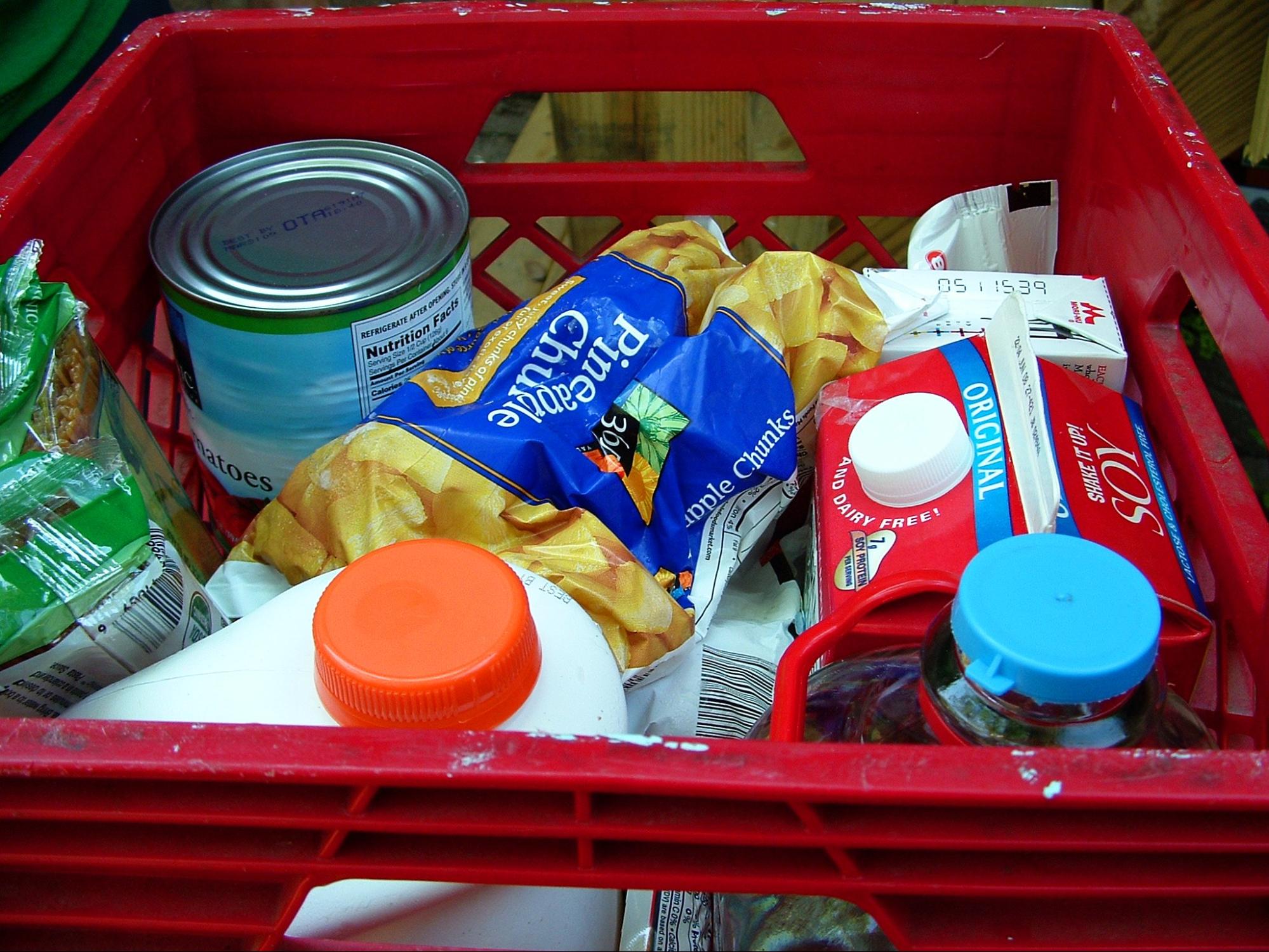 crate of groceries, including milk, juice, and veggie cans