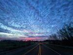blue cloudy sky at dusk with pink sunset in distance, along highway