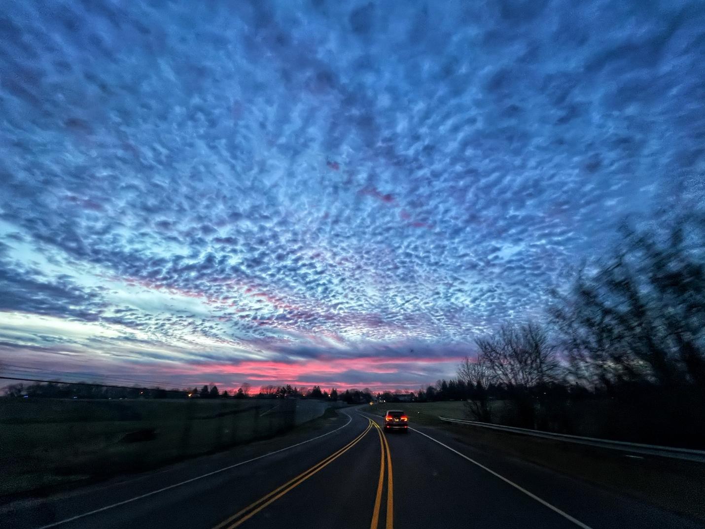 blue cloudy sky at dusk with pink sunset in distance, along highway